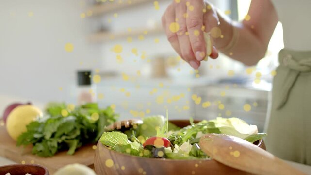 Hands entering frame starting sprinkling crumbled cheese then squeezing lemon, dressing salad