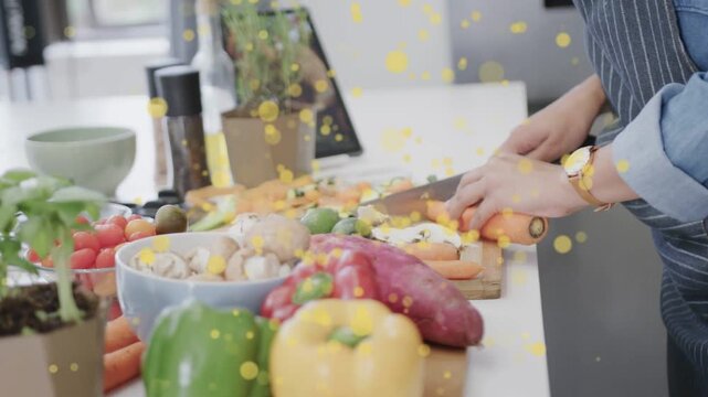 Woman placing carrot, chopping on board preparing meal with yellow bokeh overlay across counter