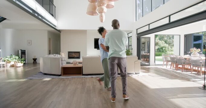 African American couple entering wide glass door, walking into living area, dancing, celebrating