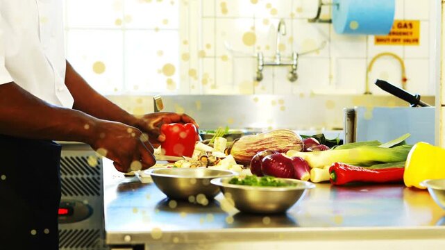 Male cook grabbing red pepper and slicing into bowl on kitchen counter, warm overlay accenting prep