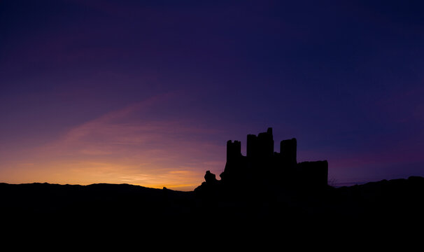 View of the silhouette of Rocca Calascio castle against a vibrant purple and orange twilight sky over the Apennine Mountains Calascio, Abruzzo, Italy.