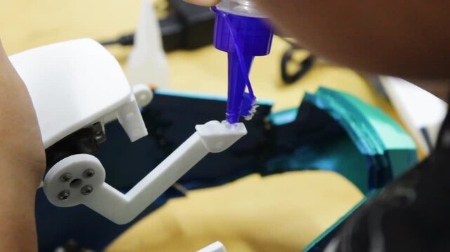 An unrecognizable boy is gluing a plastic sheet with liquid glue onto a surface for a technology project at a robotics club in Neiva, Huila, Colombia. Concept of technology and handmade