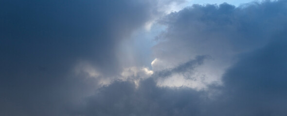 Fototapeta premium Sunbeams breaking through dark storm clouds on dramatic blue-grey sky