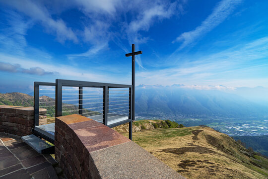View of the summit cross Santa Maria degli Angeli church on Monte Tamaro overlooking the alpine valley and distant mountains under a bright blue sky Gambarogno, Ticino, Switzerland.