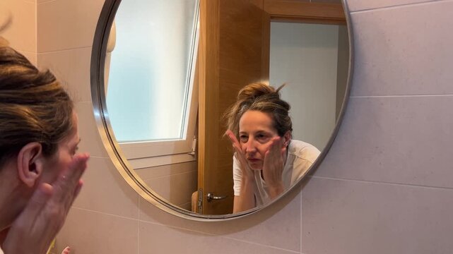 Mujer lav&aacute;ndose la cara frente al espejo del ba&ntilde;o
