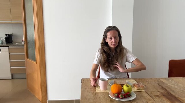 Mujer saliendo de la cocina y sent&aacute;ndose a desayunar