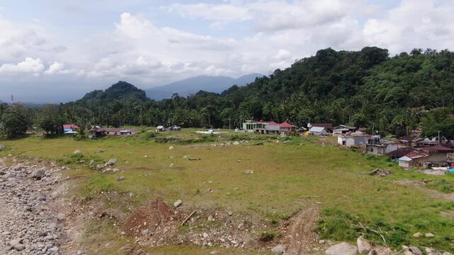 Agam, Indonesia - April 3rd 2026: Aerial Drone Push-in Toward Rural Village Settlement Nestled Against Hills in Salareh Aia: Post-Flash Flood Landscape View of Disaster-Affected Area