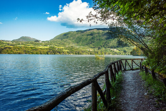 View of Bacino di Suviana with its serene water and a rustic wooden fence path under a blue sky in Metropolitan City of Bologna, Emilia-Romagna, Italy.