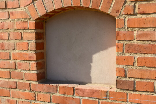 A close-up of a stone wall with a window arch. The background texture is a brick wall with a geometric pattern.