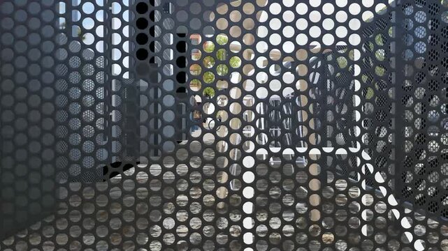 View of an urban street through a perforated metal screen with modern buildings.