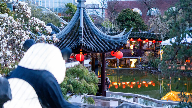 View of the Lan Su Chinese Garden featuring traditional architecture, red lanterns, and a pond with a panda statue in the foreground Portland, Oregon, United States.