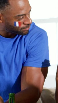 Vertical video: Bumping fists man in blue tee reacting to raised fist on sofa with flag face paint