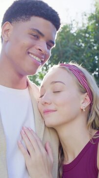 Vertical video: Placing hand on chest, couple shifting to smile for camera at park, jacket headband
