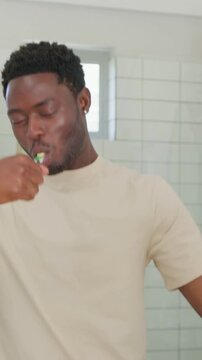 Vertical video: Grabbing green toothbrush, man brushing teeth at sink, beige tee, purple toothbrush