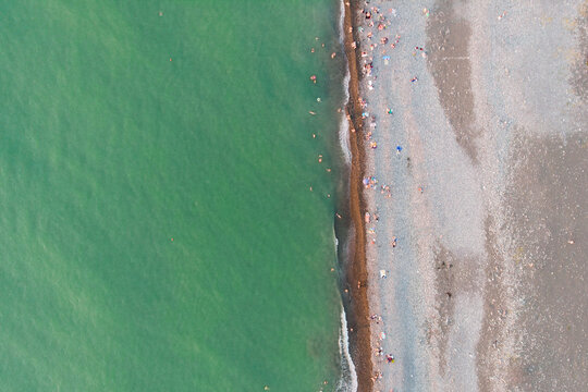 Aerial top view of turquoise sea water and pebble beach with people. Summer vacation, coastal lifestyle, minimalist nature background and tourism concepts,freedom, relaxation and travel, beach holiday