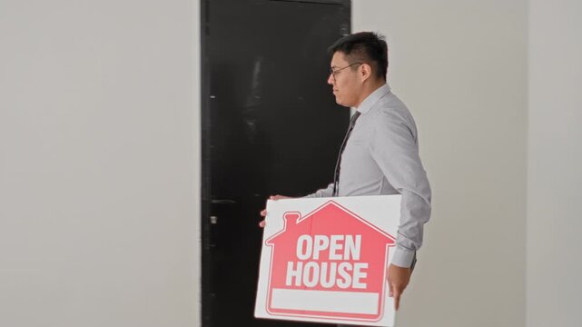 Man placing open house sign on floor inside building while wearing tie and glasses, arms crossed in later frame; confidence readiness.