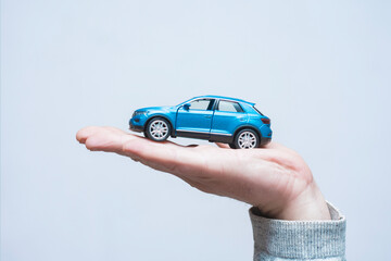 Small scale model of a modern blue suv car resting on a man palm. Concept car buying, auto insurance protection, vehicle loan accessibility and transportation gifts. © vadish