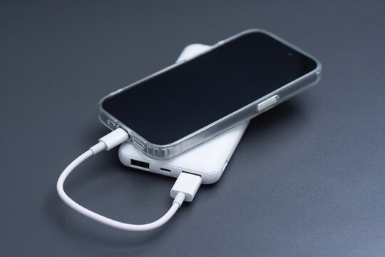 Smartphone connected to a white power bank with a USB charging cable on a dark background. Concept mobile charging, portable battery, device power and technology accessory.