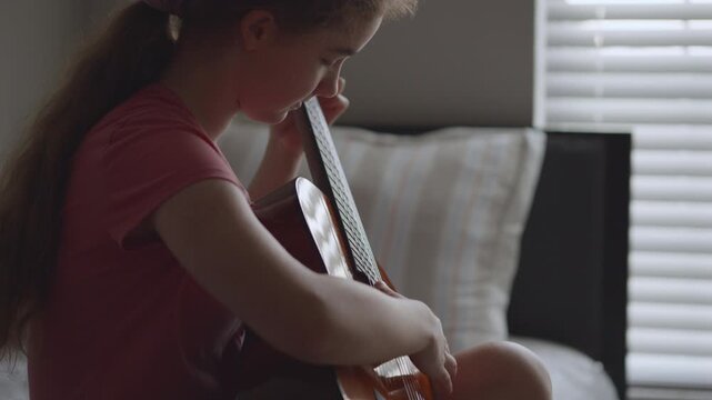 Young girl with long hair learning to play acoustic guitar at home. Portrait of young girl focused on learning guitar. Practice and musical education at home. Child leisure playing acoustic guitar.