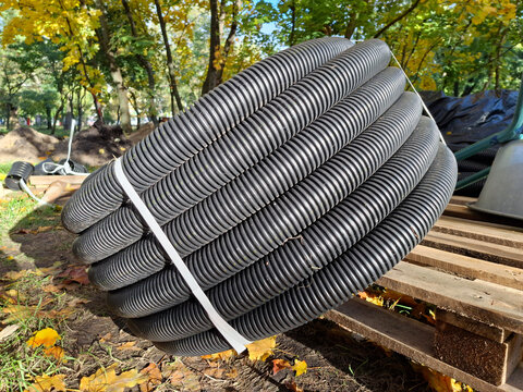 A black plastic corrugated pipe is wound into a coil lies on construction site