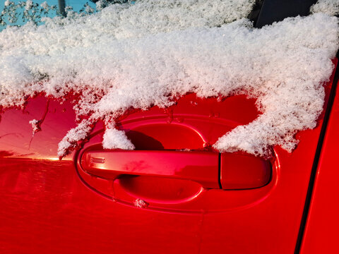 The side window and door handle of the red car are dusted with snow