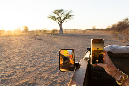 woman using smart phone to photograph baobab tree, Makgadikgadi National Park, Botswana, Africa