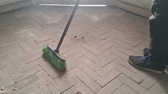 Person's legs visible as a broom sweeps across a rustic herringbone tiled floor in motion video clip