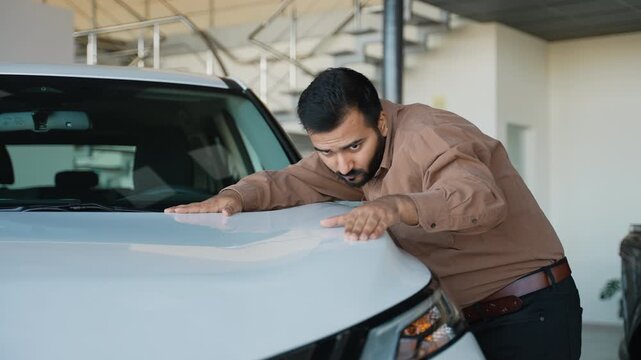 Indian man inspecting a new car hood at a dealership showroom