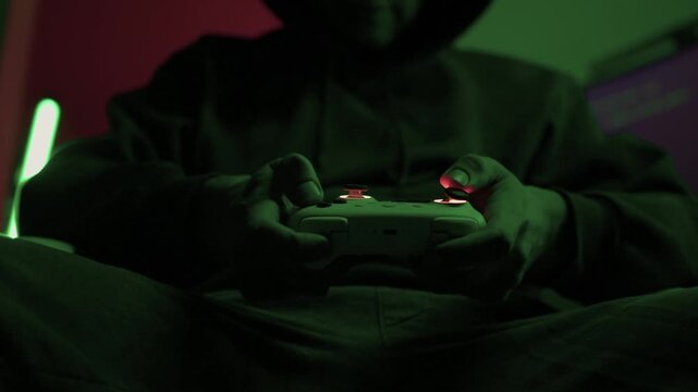 Gamer gripping red controller in dark hoodie, lowlit room with neon green PC and blurred monitor, closeup on hands and controller, tense focused mood, latenight stream atmosphere