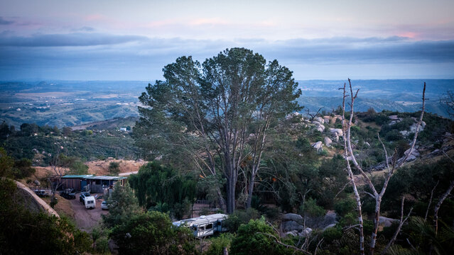View of the Splitrock Baby Oaks area featuring a large oak tree, rocky hillsides, and trailers under a twilight sky in Fallbrook, California, United States.