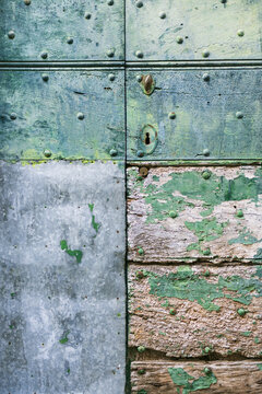 View of an old weathered wooden door with peeling green paint, metal rivets, and a galvanized metal patch in Italy.