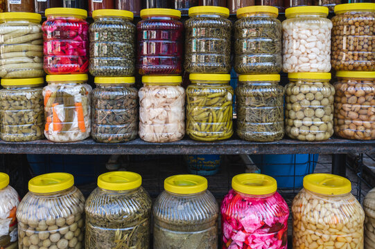 Assorted pickled vegetables are packed in glass jars with yellow lids. Traditional preserved food at a local market