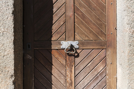 View of an old wooden door with diagonal planks and a metal knocker set in a stone frame in Italy.