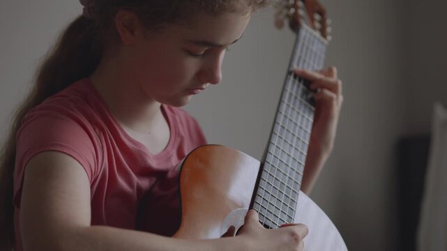Young girl with long hair learning to play acoustic guitar at home. Portrait of young girl focused on learning guitar. Practice and musical education at home. Child leisure playing acoustic guitar.