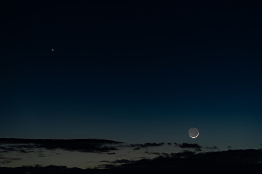 View of the crescent moon and a bright star shining in the dark night sky above a silhouette of clouds in Kyiv, Kyiv city, Ukraine.