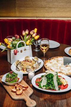Dinner table with pizza pasta carpaccio and wine. Full restaurant table spread including seafood pasta, white pizza, beef carpaccio, wine glass and tulip decoration.