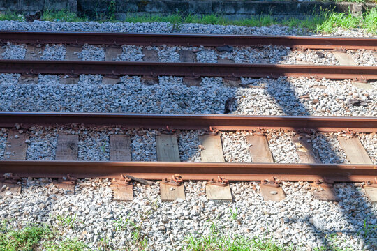 Close-up view of parallel railway tracks with steel rails, wooden sleepers, and gravel ballast, with strong sunlight and shadow contrast highlighting texture, alignment details of rail infrastructure.