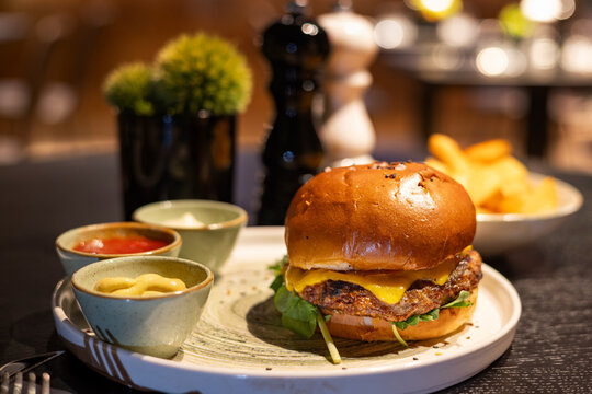 Close-up of a gourmet cheeseburger served with mustard, ketchup and fries in a cozy restaurant atmosphere, warm lighting and shallow depth of field.