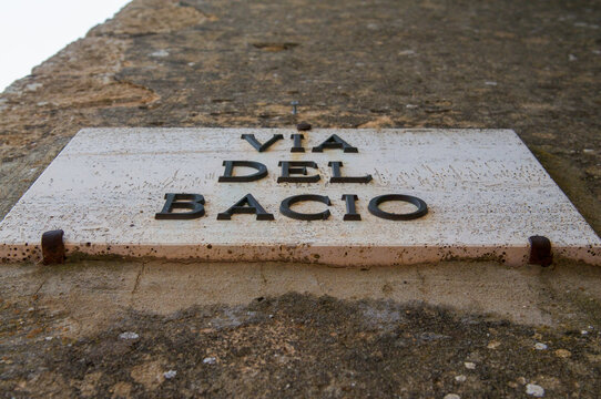White marble street sign of Via del Bacio on building facade in Pienza,Italy