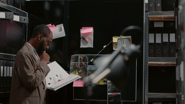 Private detective looking at evidence on board and comparing police report with criminal files. Investigator holding folder with forensic evidence, analyzing clues to conduct investigation.