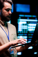 Serviceman doing system analysis, typing data on laptop of needed adjustments in supercomputers...