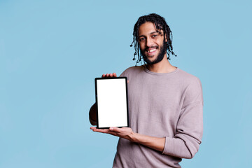 Cheerful arab man holding digital tablet with blank touchscreen and looking at camera. Smiling person showing portable device with empty white screen background for software ads © DC Studio