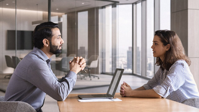 Indian male hr specialist manager, employer, boss listening female latin candidate at job interview, consulting client at office meeting. Hiring and employment, human resources, recruitment concept.