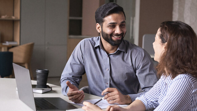 Two professionals - happy smiling indian hr manager and latin young female colleague at office meeting having fun. Mentoring Hispanic male teacher and female student in multiethnic creative space.