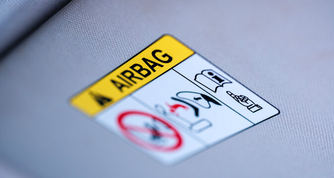 Macro close up of a yellow and white passenger airbag safety warning sticker attached permanently to the soft gray fabric sun visor inside a modern vehicle