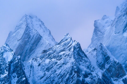 View of the sharp snow-covered peaks of the Haldi Cones under a cool blue twilight sky Khaplu, Baltistan, Pakistan.