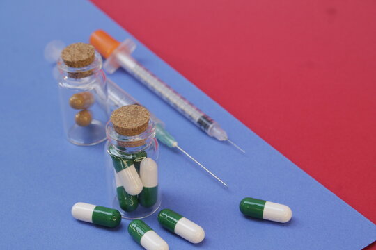 Jeringas y c&aacute;psulas para tratamiento m&eacute;dico, colocadas sobre fondo azul y rojo.