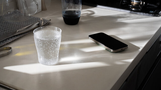 Bubbling Sparkling Water Glass Beside Smartphone on Kitchen Counter with Window Light