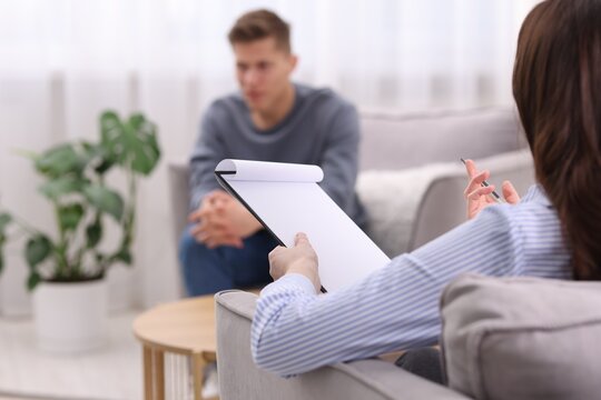 Professional psychologist making notes on clipboard during therapy session with patient indoors, selective focus
