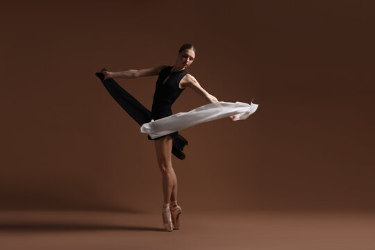 Graceful ballerina practicing dance moves with black and white veils on brown background